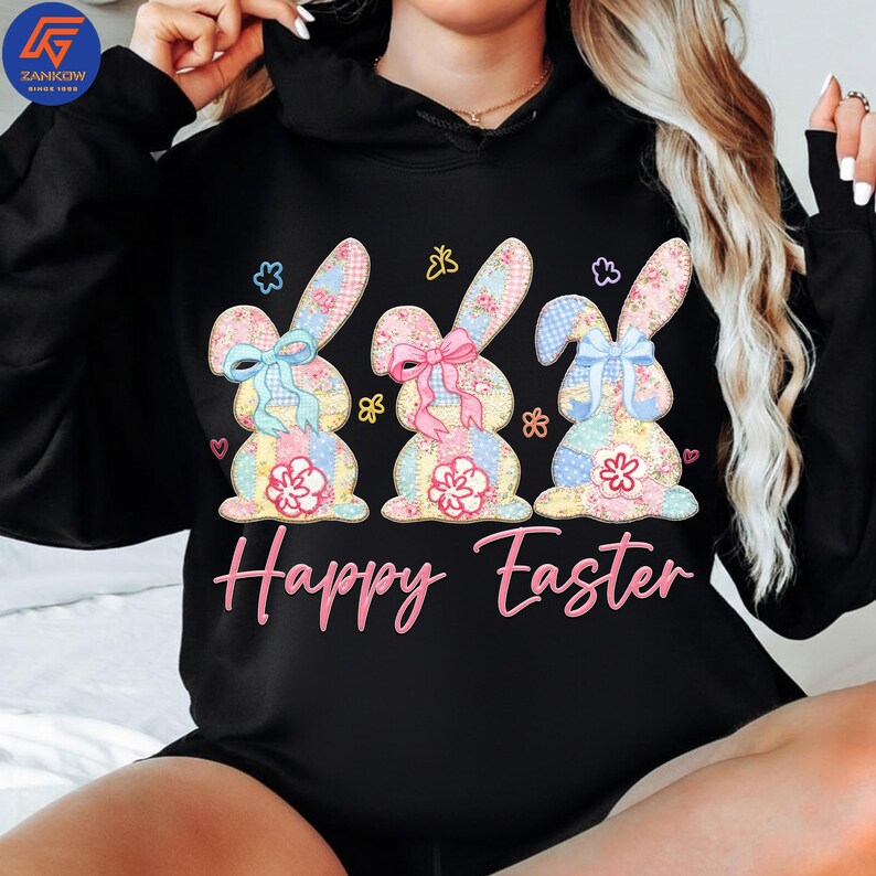 May include: Black hoodie featuring a colorful graphic of three Easter bunnies with floral patterns, bows, and the text "Happy Easter" in pink. The bunnies are in pastel colors, creating a festive and cheerful design.