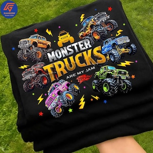 May include: Black t-shirt with a graphic of monster trucks and the phrase "Monster Trucks Are My Jam." The design showcases monster trucks in orange, yellow, red, blue, green, and pink, with lightning bolts and star details.