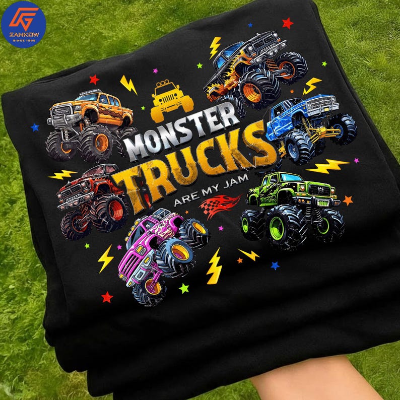 May include: Black t-shirt with a graphic of monster trucks and the phrase "Monster Trucks Are My Jam." The design showcases monster trucks in orange, yellow, red, blue, green, and pink, with lightning bolts and star details.