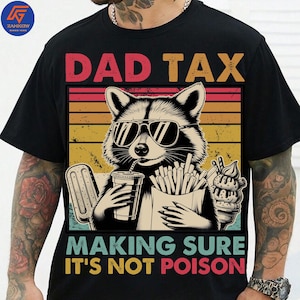 May include: Black t-shirt with a raccoon wearing sunglasses, holding a drink, fries, and ice cream. The text "DAD TAX" is above the raccoon, and "MAKING SURE IT'S NOT POISON" is below.