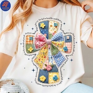 以下が含まれることがあります： クリーム色のTシャツ。パッチワークの十字架のデザインで、花柄とギンガムチェックの模様が特徴です。「For God so loved the world」というテキストが含まれています。装飾要素には花とリボンが含まれています。