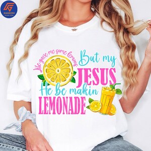 May include: White t-shirt with a colorful graphic design. The design features a sliced lemon, a glass of lemonade, and the text "Life gave me some lemons But my JESUS He be makin LEMONADE."