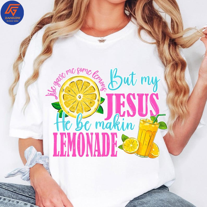 May include: White t-shirt with a colorful graphic design. The design features a sliced lemon, a glass of lemonade, and the text "Life gave me some lemons But my JESUS He be makin LEMONADE."