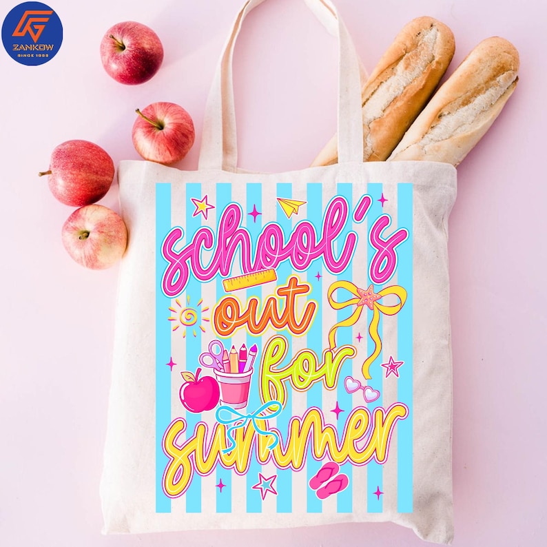 May include: Cream-colored tote bag with blue vertical stripes and the words "School's Out For Summer" in pink, orange, and yellow. The bag contains two baguettes and is surrounded by red apples.