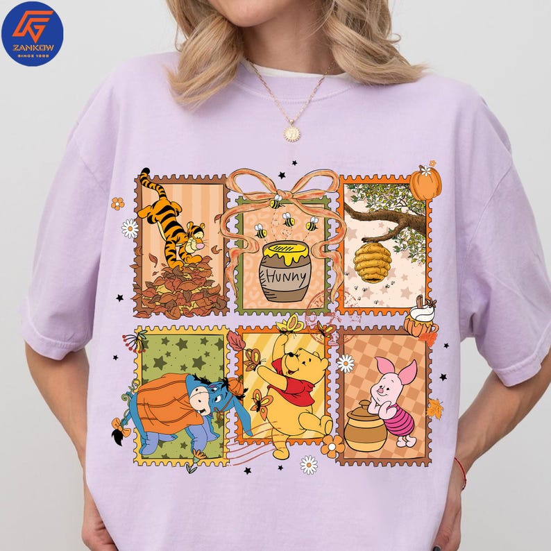 May include: A lilac t-shirt with a colourful graphic of Winnie the Pooh characters in postage stamp designs. The design includes Tigger, Winnie the Pooh, Piglet, Eeyore, a honey pot, and a beehive.