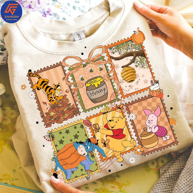 May include: Cream-coloured sweatshirt with a colourful graphic of Winnie the Pooh characters in postage stamp designs. The design includes Tigger, Winnie the Pooh, Piglet, Eeyore, a honey pot, and a beehive.