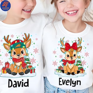 May include: White long-sleeved shirts with Christmas reindeer graphics. One shirt features a reindeer wearing a hat and scarf, with the name "David" below. The other shirt shows a reindeer with a bow and scarf, with the name "Evelyn".
