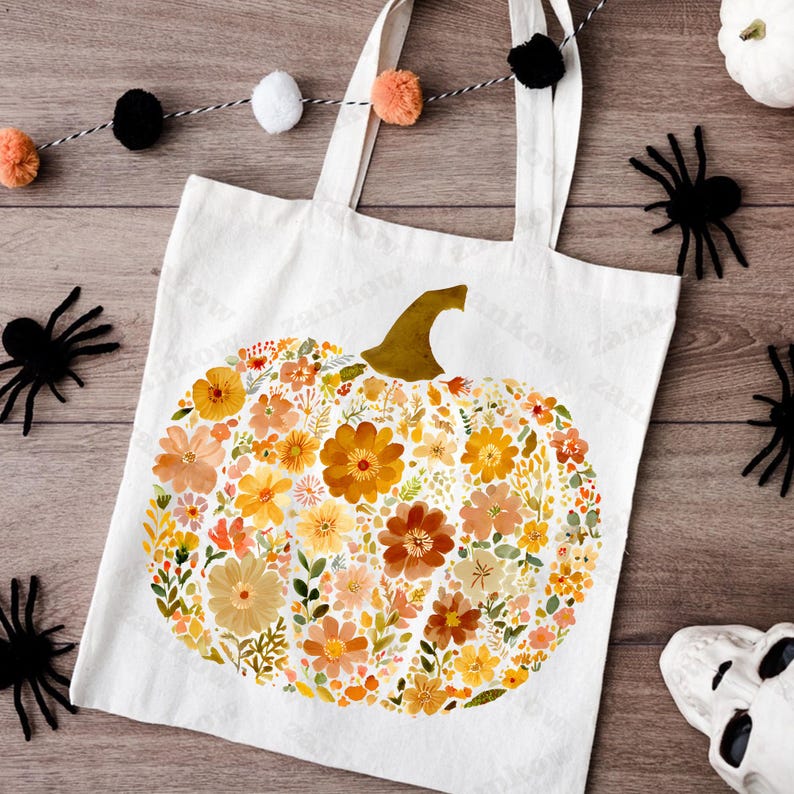 May include: A white tote bag featuring a floral pumpkin design in shades of orange, yellow, and brown. The bag has two white handles and is decorated with black spiders and a garland of pom-poms, perfect for fall or Halloween.