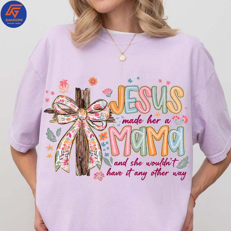 May include: A lilac t-shirt featuring the text "JESUS made her a MAMA and she wouldn't have it any other way." The design includes a wooden cross with a floral bow and colourful floral accents.