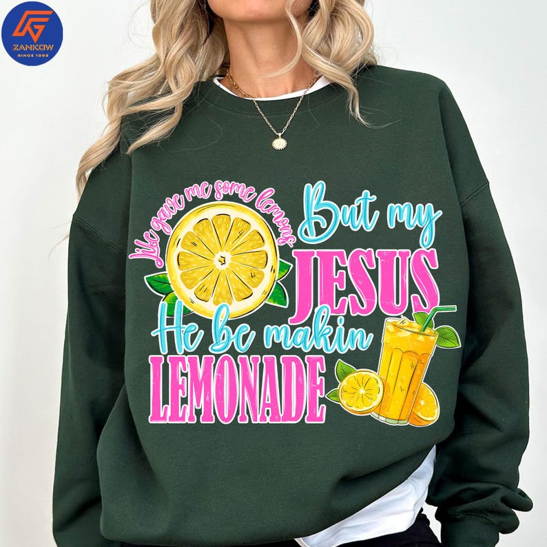 May include: Dark green sweatshirt with the text "They gave me some lemons But my JESUS He be makin LEMONADE" in pink and blue. The design includes a lemon slice and a glass of lemonade.