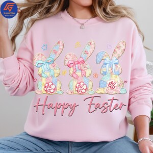 May include: A light pink sweatshirt featuring three patchwork bunny rabbits with floral and gingham patterns. Each bunny has a bow and a flower. The words "Happy Easter" are written in pink script below the bunnies.