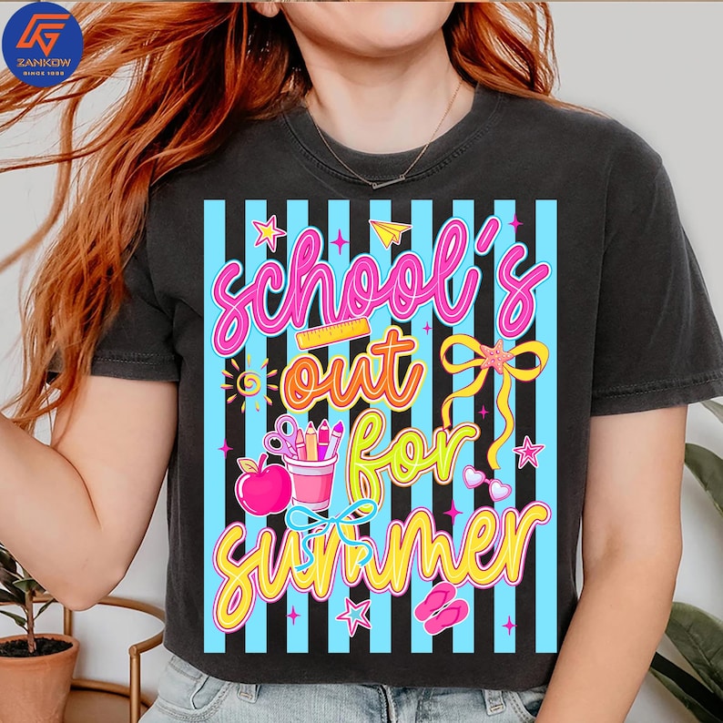 May include: Dark gray t-shirt with a colorful graphic that says "School's out for Summer." The design includes a pink apple, pencils, scissors, and stars. The text is in pink, yellow, and orange, with a blue striped background.