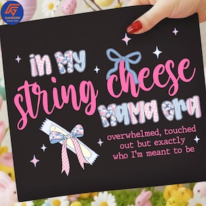 May include: Black sign with the text "in My string cheese Mama era" in pink and blue script. The sign also includes the text "overwhelmed, touched out but exactly who I'm meant to be". Decorative bows and stars are also featured.