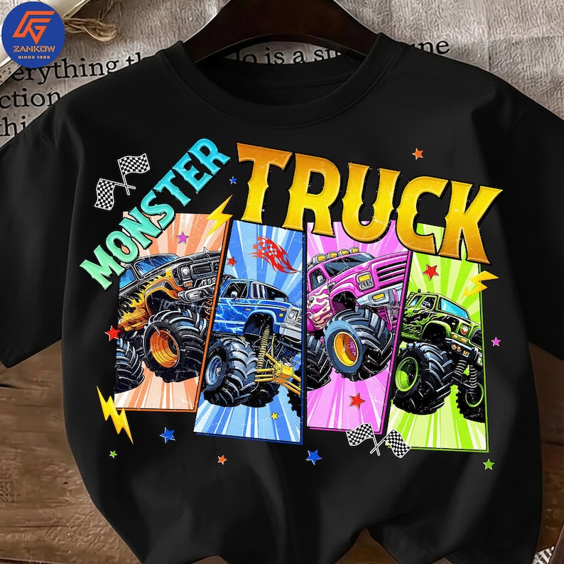 May include: Black t-shirt featuring the words "MONSTER TRUCK" in large, colorful letters. The shirt displays four monster trucks in different colors: yellow, blue, pink, and green. Each truck is set against a vibrant background with stars and checkered flags.