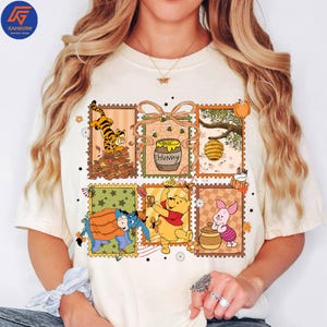 May include: Cream-coloured t-shirt featuring a colourful graphic of Winnie the Pooh characters in postage stamp designs. The design includes Tigger, Pooh, Eeyore, Piglet, a honey pot, and a beehive. The word "Hunny" is also visible.