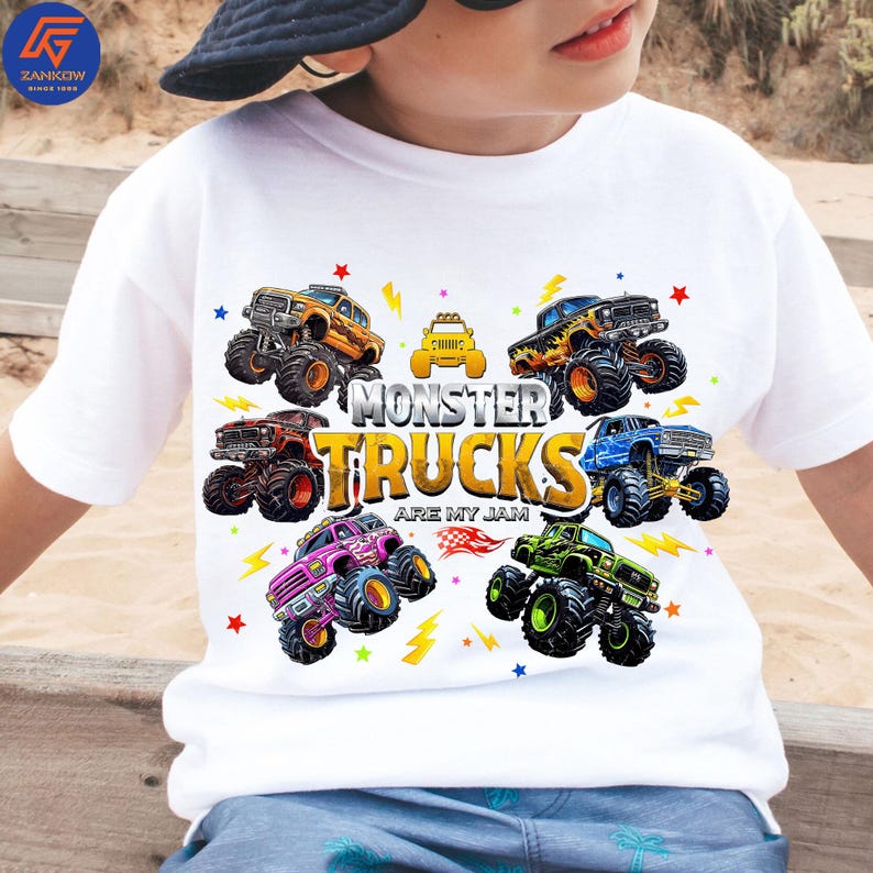 May include: White t-shirt with a vibrant graphic of monster trucks. The design showcases monster trucks in orange, black, red, pink, blue, and green, accompanied by the text "MONSTER TRUCKS ARE MY JAM".