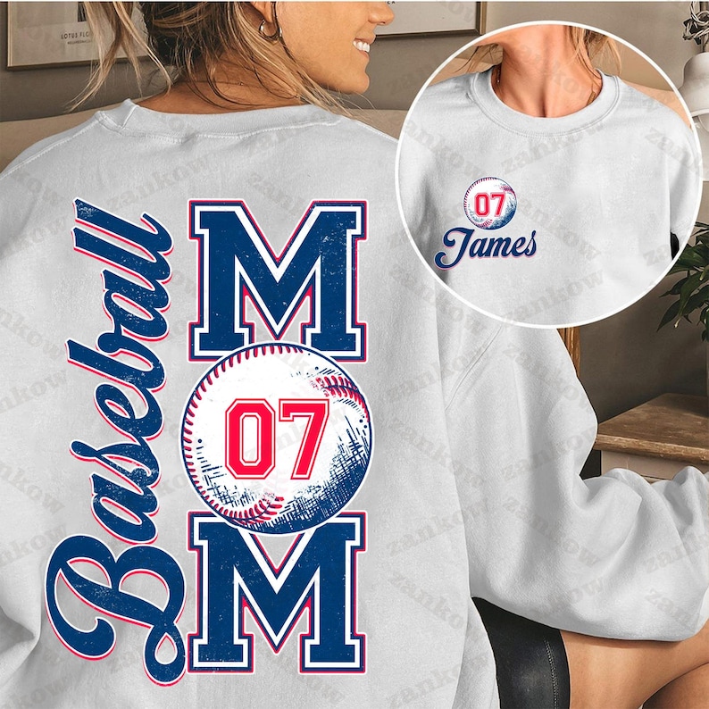 May include: White sweatshirt with a baseball-themed design. The text "Baseball Mom" is printed in blue and red with a baseball graphic featuring the number "07".