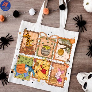 May include: White tote bag with a colourful graphic of Winnie the Pooh characters in a postage stamp design. The bag has two white handles and is decorated with Halloween-themed accents, including spiders and a garland.