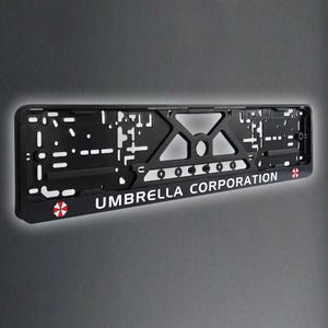 Może przedstawiać: Czarna metalowa ramka na tablicę rejestracyjną z napisem "Umbrella Corporation" i czerwono-białym symbolem biohazardu.