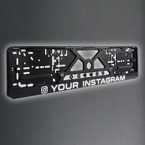 Può includere: Telaio per targa nero con logo Instagram bianco e il testo "YOUR INSTAGRAM".
