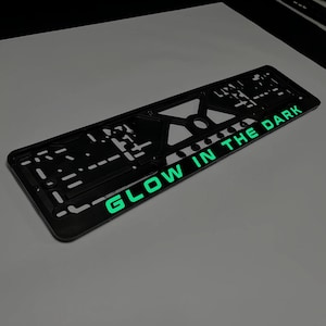 Könnte beinhalten: Schwarzer Nummernschildrahmen aus Kunststoff mit der Aufschrift "GLOW IN THE DARK" in grüner Schrift.