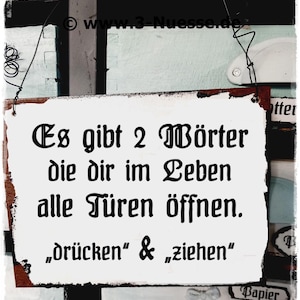 Puede incluir: Un cartel blanco con texto negro que dice "Es gibt 2 Wörter die dir im Leben alle Türen öffnen. "drücken" & "ziehen" ". El cartel está colgado de un gancho de metal oxidado.