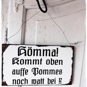 Pode incluir: Um sinal de madeira branco com texto preto que diz "Gomma! Kommt oben auffe Bommes noch matt bei!" com o texto "©BNUESSE" na parte inferior.