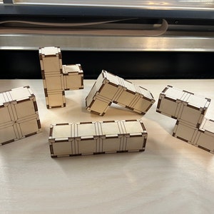 Könnte beinhalten: Fünf Holzteile eines Puzzles mit geometrischem Muster. Die Teile sind aus hellem Holz mit braunen Linien und liegen auf einer hellen Holzoberfläche.