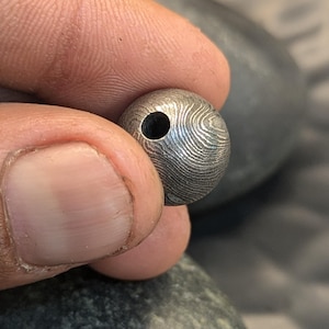 May include: A silver metal bead with a textured surface and a small hole in the center.