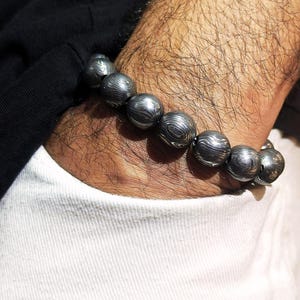 May include: A bracelet made of dark grey, round beads with a swirling pattern. The beads are strung together on a silver chain.