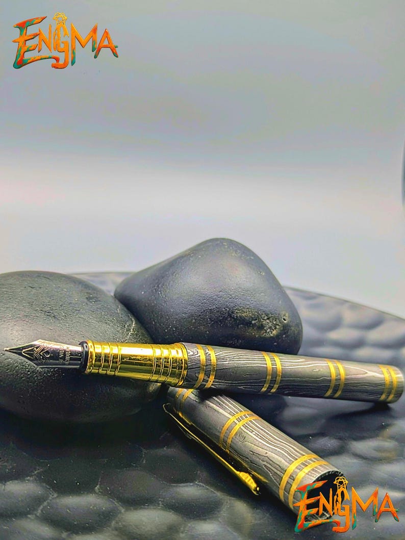 以下が含まれることがあります： 黒と金のデザインの高級万年筆。 ペンは、金色のアクセントと金のペン先を備えた模様のバレルを備えています。 ペンはキャップを横に置いて表示され、左上隅に「Enigma」という単語があります。