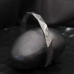 May include: A silver bracelet with a geometric pattern. The bracelet is made of a metal with a hammered finish.