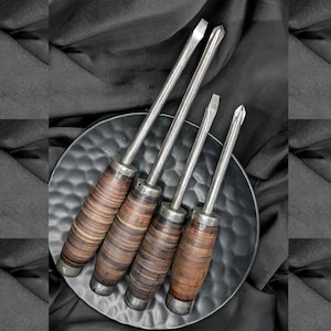 May include: Four vintage screwdrivers with wooden handles. The handles are striped with brown and black wood. The screwdrivers are arranged on a black plate.