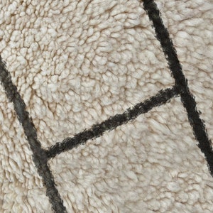 May include: A thick, cream-colored shag rug featuring a geometric pattern of intersecting dark charcoal lines. The texture is dense and plush, with long, soft fibers creating a high-pile surface that highlights the contrast between the light base and the dark, linear grid design.