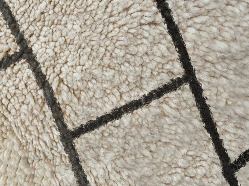 May include: A thick, cream-colored shag rug featuring a geometric pattern of intersecting dark charcoal lines. The texture is dense and plush, with long, soft fibers creating a high-pile surface that highlights the contrast between the light base and the dark, linear grid design.