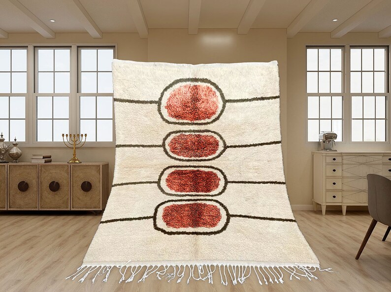 May include: A cream-coloured area rug featuring four vertically aligned, oval-shaped motifs in shades of rust red, each outlined in dark brown. The rug includes horizontal dark brown lines extending from the ovals and white fringe at the bottom.
