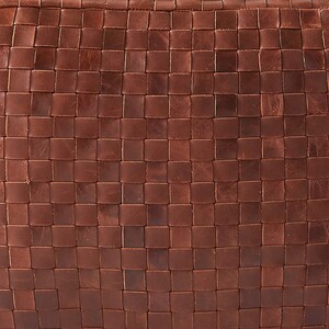 May include: A brown leather surface featuring a tight, uniform woven grid pattern. The material displays natural variations in tone and texture across the interlocking square strips, creating a consistent, dense, and tactile geometric design.