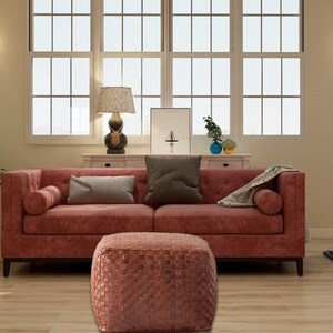 May include: A square, woven leather ottoman with a textured, grid-like surface in a deep reddish-brown tone, positioned in front of a matching reddish-brown tufted sofa with two bolster pillows and two rectangular throw pillows.