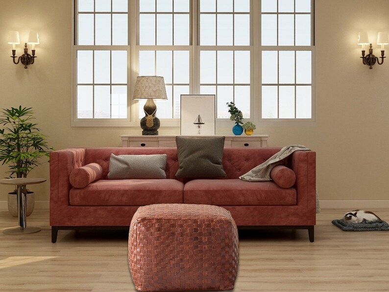 May include: A square, woven leather ottoman with a textured, grid-like surface in a deep reddish-brown tone, positioned in front of a matching reddish-brown tufted sofa with two bolster pillows and two rectangular throw pillows.