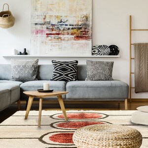 May include: A rectangular area rug featuring a cream-coloured base with dark brown horizontal lines and three prominent, textured, circular motifs in shades of deep red and orange, positioned centrally on the floor in a living room setting.