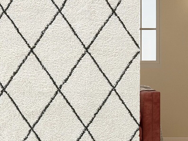 May include: A plush, off-white area rug featuring a repeating black diamond grid pattern. The surface has a thick, textured pile, and the dark lines of the geometric design appear slightly irregular, resembling a hand-drawn or sketched aesthetic.
