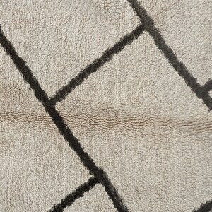 May include: A textured rug featuring a cream-colored base with a pattern of thick, dark brown intersecting lines that form irregular geometric shapes across the surface. The material has a dense, soft, and slightly shaggy pile appearance.