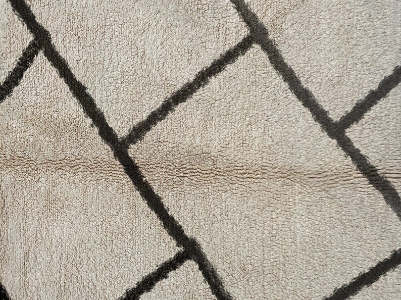 May include: A textured rug featuring a cream-colored base with a pattern of thick, dark brown intersecting lines that form irregular geometric shapes across the surface. The material has a dense, soft, and slightly shaggy pile appearance.