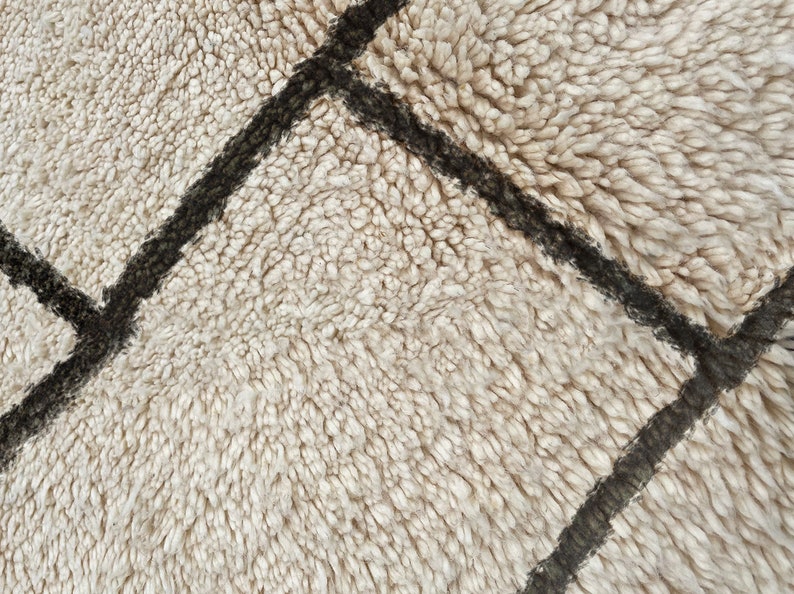 May include: A high-pile rug featuring a thick, cream-colored shag texture with dark brown, hand-drawn geometric lines intersecting across the surface. The dense, soft fibers create a deep, plush appearance with a visible grid pattern.