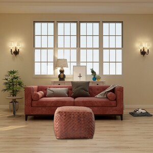 May include: A deep red tufted sofa with bolster pillows and a matching square woven ottoman. The sofa features a dark gray throw pillow and a light gray blanket, positioned in a room with light wood flooring and large windows.
