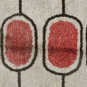 May include: A textured rug featuring a repeating pattern of vertical black lines connecting rounded rectangular shapes. Each shape contains a solid, deep red centre surrounded by a light grey, plush, high-pile fabric background.