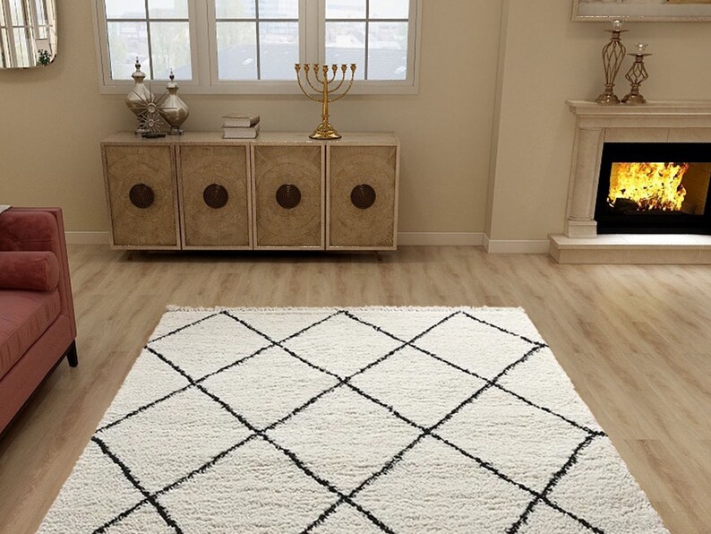 May include: A rectangular area rug featuring a thick, cream-colored shag texture with a prominent black diamond grid pattern. The rug is positioned on a light-toned wood floor, showcasing a soft, plush pile and clean, geometric lines.