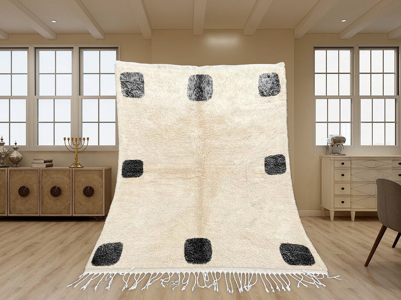 May include: A rectangular area rug featuring a cream-colored base with a repeating pattern of nine dark gray, textured square shapes arranged in a grid. The rug has a thick, plush pile and is finished with white fringe along the bottom edge.