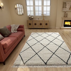 May include: A rectangular area rug featuring a cream-colored shaggy pile with a repeating black diamond grid pattern. The rug is finished with short, straight fringe along the edges, providing a textured surface for the living room floor.