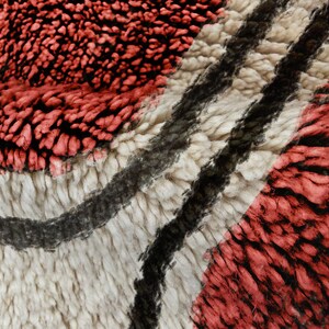 May include: A thick, high-pile rug featuring a textured pattern of deep red, cream, and black fibres. The surface displays a dense, shaggy weave with undulating dark lines that contrast against the lighter cream and vibrant red sections.